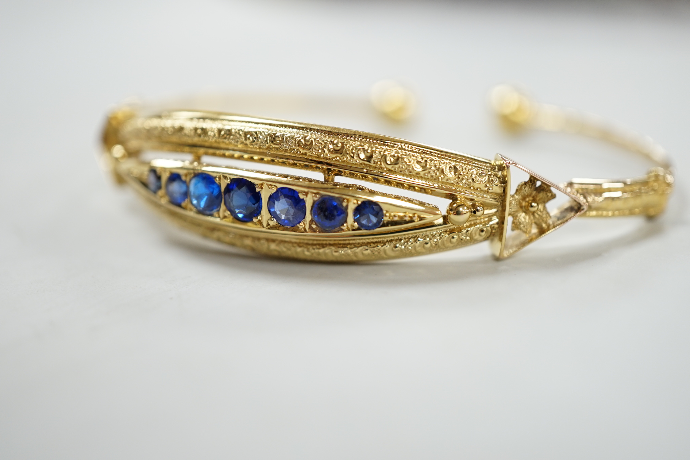 A 750 yellow metal and graduated seven stone sapphire?, paste and doublet set open work bangle, gross weight 12.1 grams.
